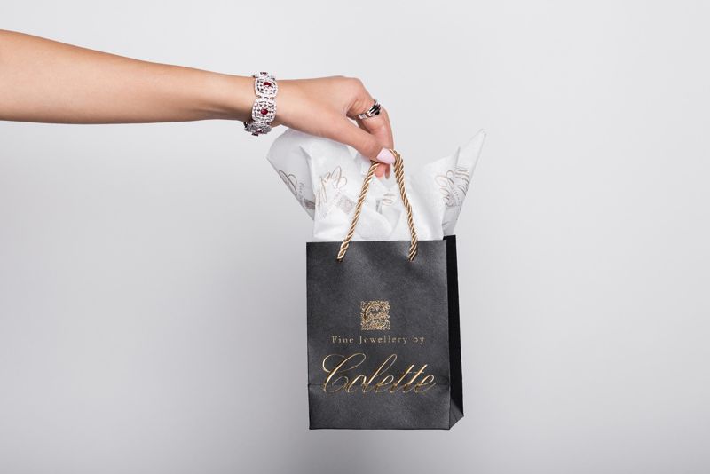 A jewelled hand holding a Fine Jewellery By Colette gift bag